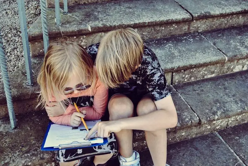 Two children leaning over a clipboard, working through a problem together